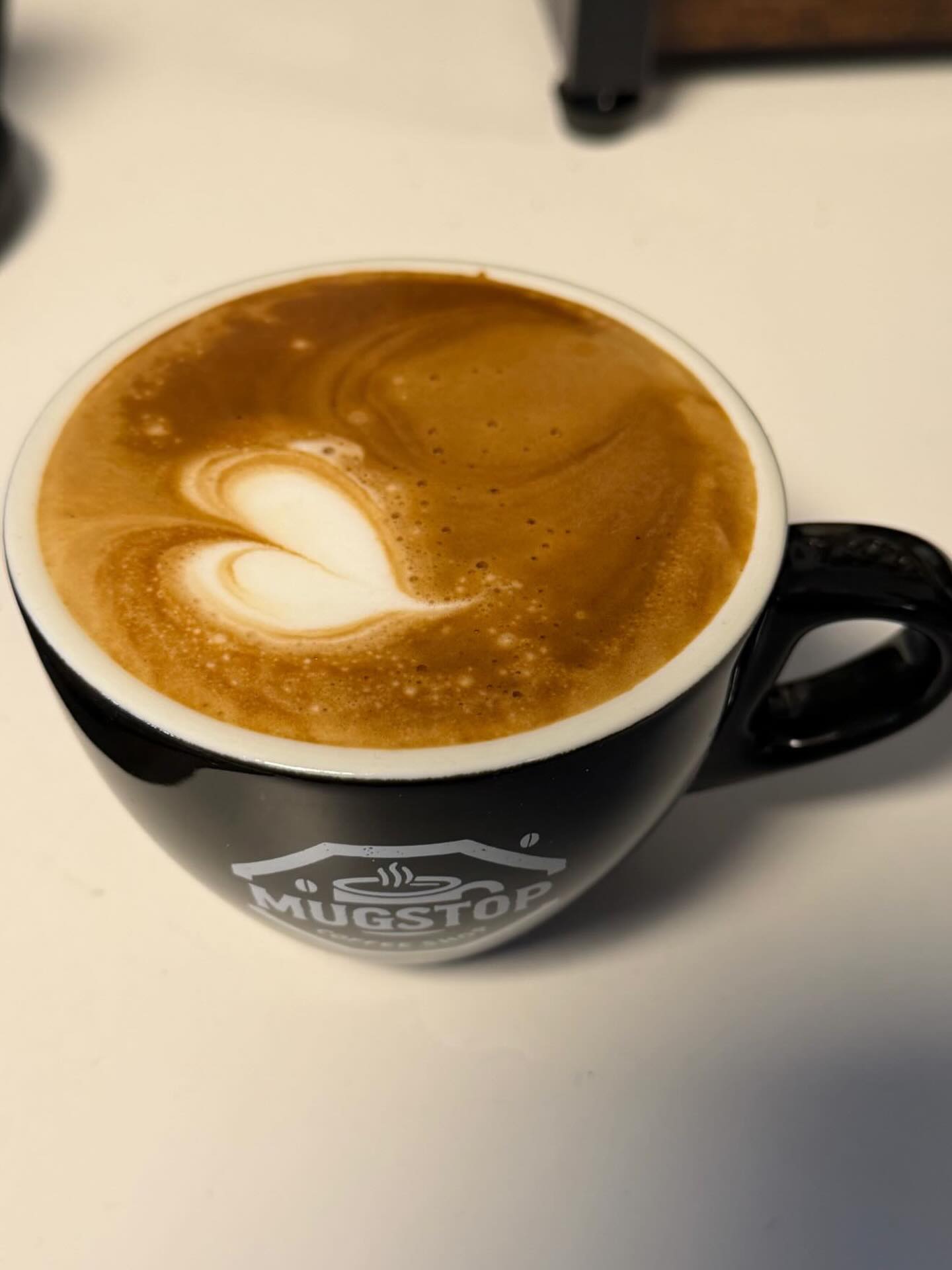 Flat white with heart-shaped latte art in a black Mugstop cup